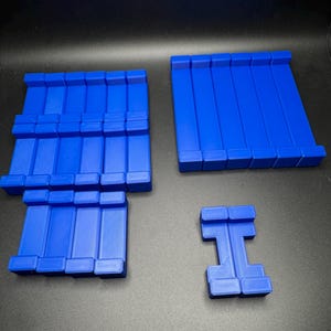 May include: A set of blue plastic building blocks. The set includes a large rectangular block, a smaller rectangular block, and a block shaped like the letter 'I'.