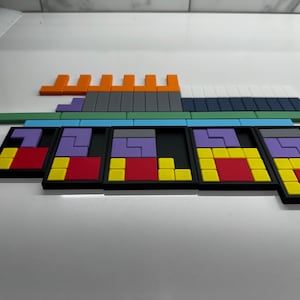 May include: A set of five colorful puzzle trays with different colored blocks in each tray. The trays are black with a yellow border. The blocks are red, yellow, purple, and gray.