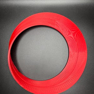 May include: A red plastic ring with a smooth, slightly textured surface. The ring is thick and has a large inner diameter.