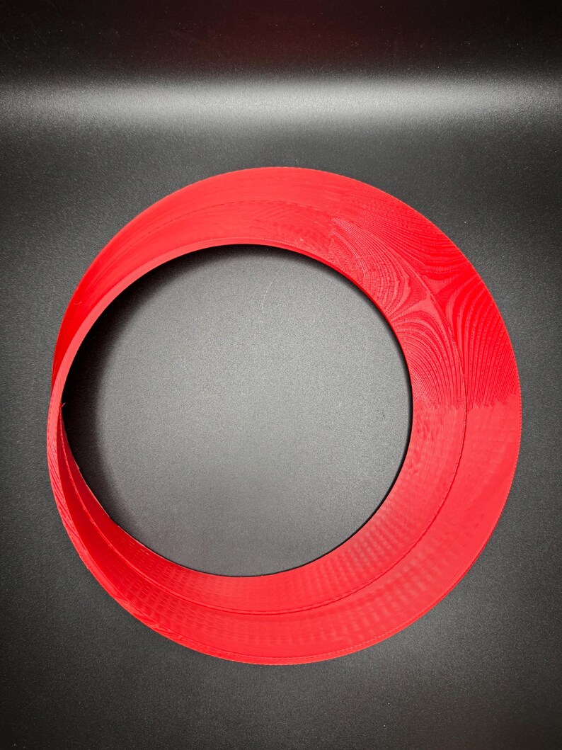 May include: A red plastic ring with a smooth, slightly textured surface. The ring is thick and has a large inner diameter.