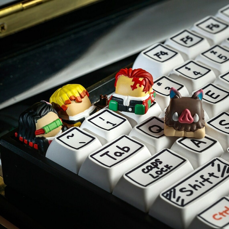 May include: Four colorful keycaps featuring characters from the anime Demon Slayer. The keycaps are placed on a black keyboard with white keys. The keys are labeled with the letters "Q", "A", "Tab", "Caps Lock", and "Shift".