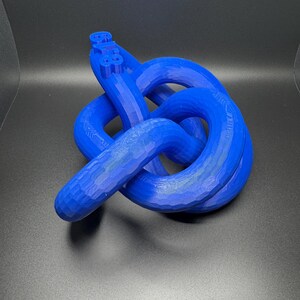 May include: A blue 3D printed knot sculpture. The knot is made of a single piece of plastic and is tied in a complex pattern.