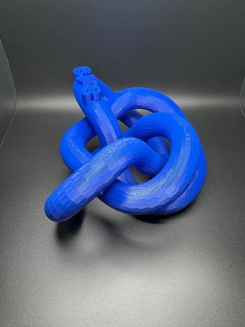 May include: A blue 3D printed knot sculpture. The knot is made of a single piece of plastic and is tied in a complex pattern.
