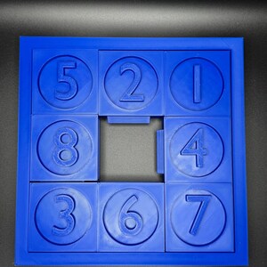 May include: A blue plastic puzzle with nine circular pieces, each with a number from 1 to 8. The puzzle is missing the number 9 piece.