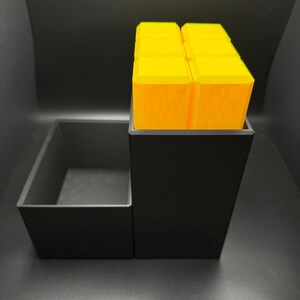 May include: A black organizer with a removable tray and a stack of bright yellow cubes. The organizer is made of plastic and has a modern design.