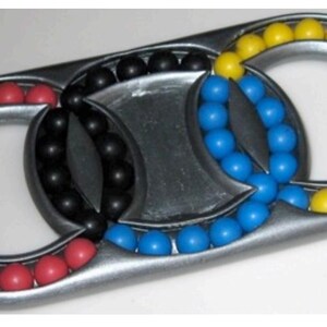 May include: A metal puzzle with three interlocking rings. Each ring contains a series of colored balls: red, black, blue, and yellow. The puzzle has a silver finish and a unique design.