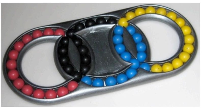 May include: A metal puzzle with three interlocking rings. Each ring contains a series of colored balls: red, black, blue, and yellow. The puzzle has a silver finish and a unique design.