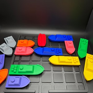 Op de afbeelding: Een set kleurrijke speelgoedbootjes op een zwart rooster speelbord. De bootjes zijn gemaakt van plastic en zijn in verschillende kleuren, waaronder rood, oranje, geel, groen, blauw en paars.