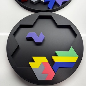 May include: A circular puzzle board with a hexagonal center. The board is black and has a variety of colorful geometric shapes that fit into the center. The shapes are purple, blue, yellow, green, gray, and pink.