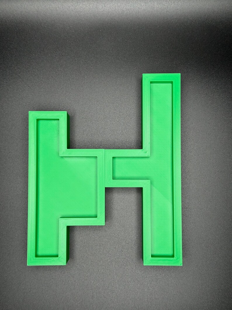 May include: A green plastic letter H puzzle piece. The letter is made up of four separate pieces that fit together.