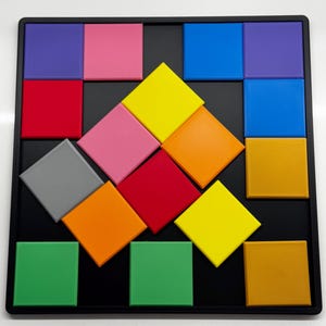 Pu&ograve; includere: Un tabellone da puzzle quadrato nero con tessere quadrate e a forma di diamante di diversi colori. Le tessere sono disposte in un motivo con una forma di diamante al centro. I colori delle tessere sono rosso, arancione, giallo, verde, blu, viola, rosa e grigio.