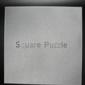 May include: A silver square puzzle with the text "Square Puzzle" printed on the front.
