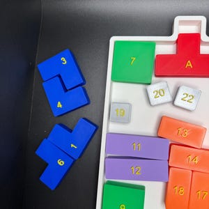Op de afbeelding: Een wit dienblad met verschillende gekleurde tegels. De tegels zijn genummerd van 1 tot 22, met de letter A, en zijn gerangschikt in een rasterpatroon. De tegels zijn gemaakt van plastic en hebben een gladde, glanzende afwerking.