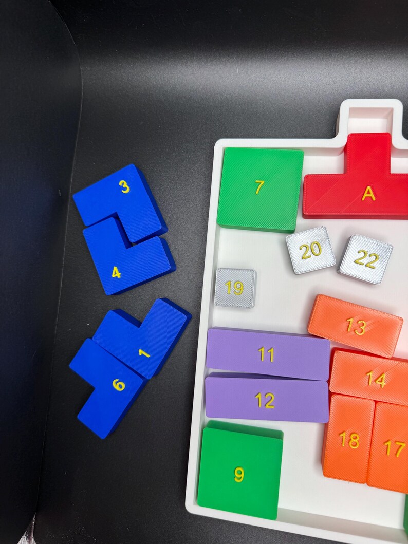 Op de afbeelding: Een wit dienblad met verschillende gekleurde tegels. De tegels zijn genummerd van 1 tot 22, met de letter A, en zijn gerangschikt in een rasterpatroon. De tegels zijn gemaakt van plastic en hebben een gladde, glanzende afwerking.