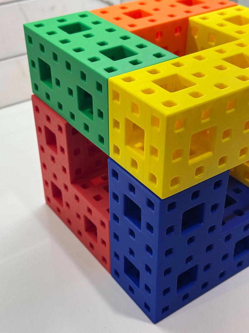 May include: A multi-colored cube made of interlocking plastic pieces. The cube is made of four different colors: green, yellow, red, and blue.