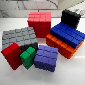May include: A set of colorful, geometric blocks made of plastic. The blocks are in various sizes and shapes, including squares, rectangles, and cubes. The blocks are arranged in a pyramid shape, with the largest block at the bottom and the smallest block at the top.
