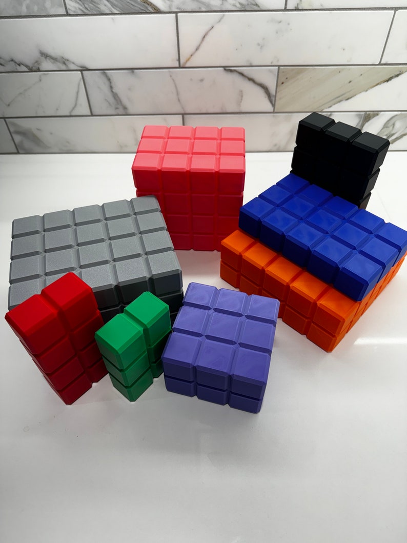 May include: A set of colorful, geometric blocks made of plastic. The blocks are in various sizes and shapes, including squares, rectangles, and cubes. The blocks are arranged in a pyramid shape, with the largest block at the bottom and the smallest block at the top.
