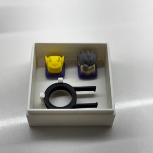 May include: A white box containing a black ring and two keycaps. One keycap is yellow and the other is grey.