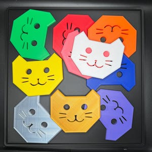 May include: A collection of colorful cat-shaped puzzle pieces in green, red, orange, pink, white, blue, yellow, silver, gold, and purple. Each piece has a smiling face with eyes, a nose, and whiskers.
