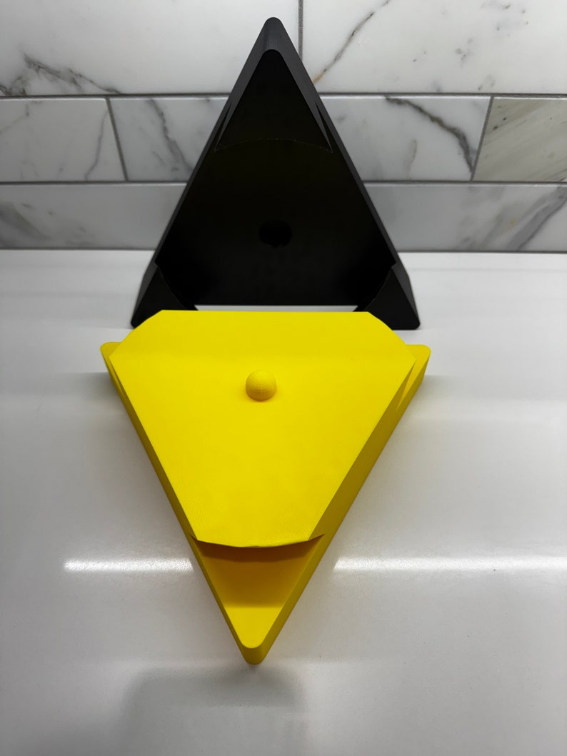 May include: A yellow triangular box with a lid and a small round knob on top. The box is sitting on top of a black triangular box.