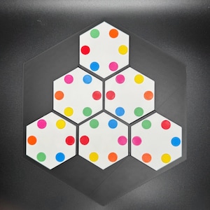 May include: A hexagonal game board with six white hexagonal tiles, each with six colored dots. The dots are red, yellow, blue, green, pink, and orange.