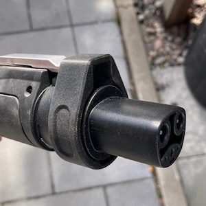 May include: Close-up of a black electric vehicle charging connector with three prongs.