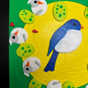 May include: A colorful, 3D-printed puzzle featuring a blue and white bird, white sheep-like figures, and green spotted eggs on a yellow and green background. The puzzle has a textured surface and a playful design.