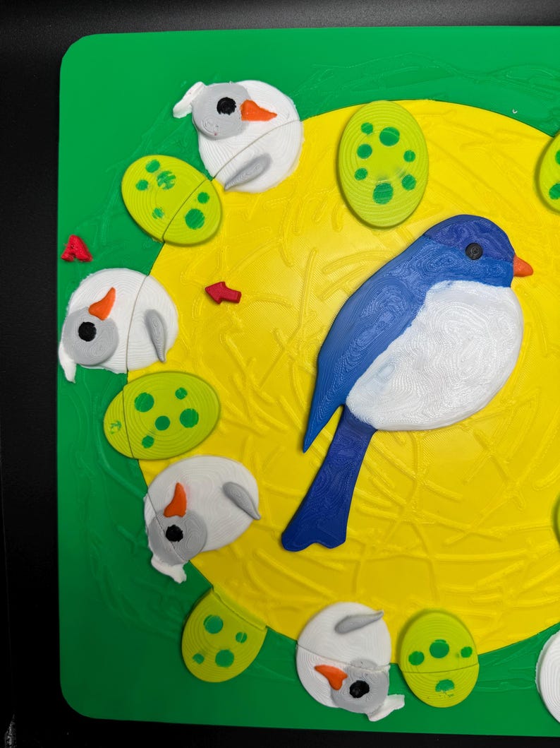 May include: A colorful, 3D-printed puzzle featuring a blue and white bird, white sheep-like figures, and green spotted eggs on a yellow and green background. The puzzle has a textured surface and a playful design.