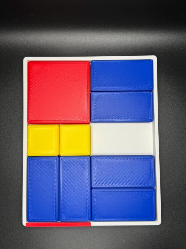 Op de afbeelding: Een wit dienblad met een geometrisch patroon in rood, geel en blauw. Het dienblad is verdeeld in negen secties, elk met een blok in een andere kleur.