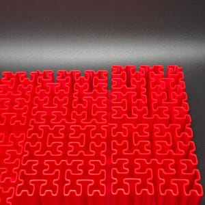 May include: A red plastic puzzle mat with interlocking pieces. The mat is made up of a grid of small squares, each with a unique shape.