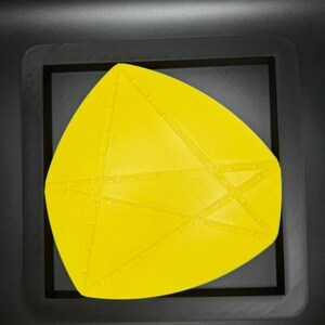 K&ouml;nnte beinhalten: Eine gelbe geometrische Form mit einer strukturierten Oberfl&auml;che, in einem schwarzen Rahmen.