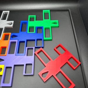 K&ouml;nnte beinhalten: Eine Sammlung farbenfroher, ineinandergreifender Puzzleteile in verschiedenen Formen und Farben, darunter Rot, Gr&uuml;n, Blau und Lila. Die Teile sind auf einer dunklen Oberfl&auml;che angeordnet und zeigen ihre geometrischen Designs.