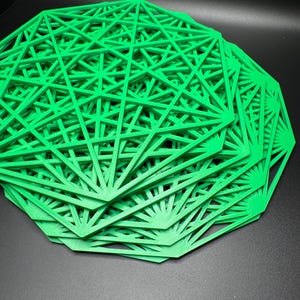 May include: A stack of green geometric, laser-cut, decorative coasters. The coasters are made of a thin, rigid material and have a delicate, intricate design.