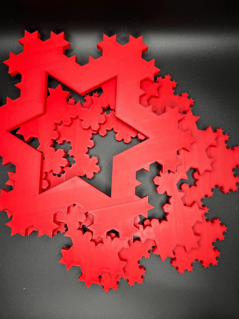 May include: A red 3D printed fractal snowflake design. The snowflake is made up of multiple layers of stars, each with a different number of points. The design is intricate and detailed.