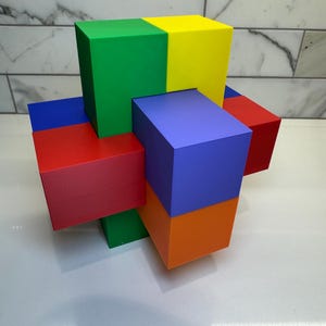 May include: A colorful wooden puzzle with six blocks in red, blue, green, yellow, orange, and purple. The blocks are arranged in a cross shape.