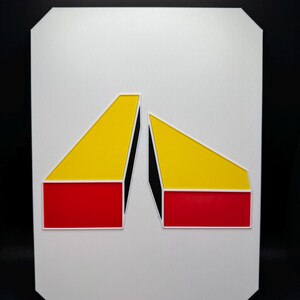 May include: Geometric abstract art piece featuring two angled shapes. The shapes are composed of red, yellow, and black blocks, set against a white background. The artwork is mounted on a white, rectangular board with rounded corners.