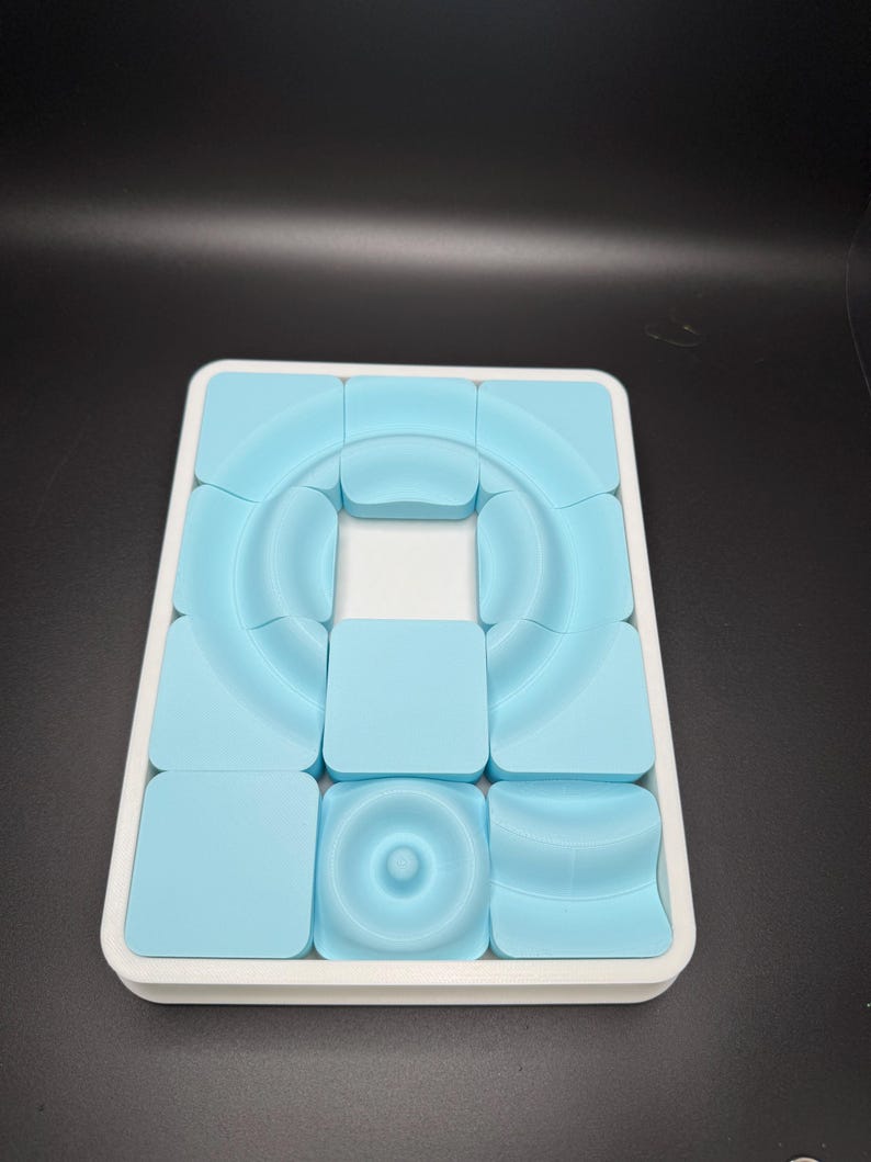 May include: A white tray with a blue puzzle inside. The puzzle is made up of 12 square pieces with different shapes and textures.