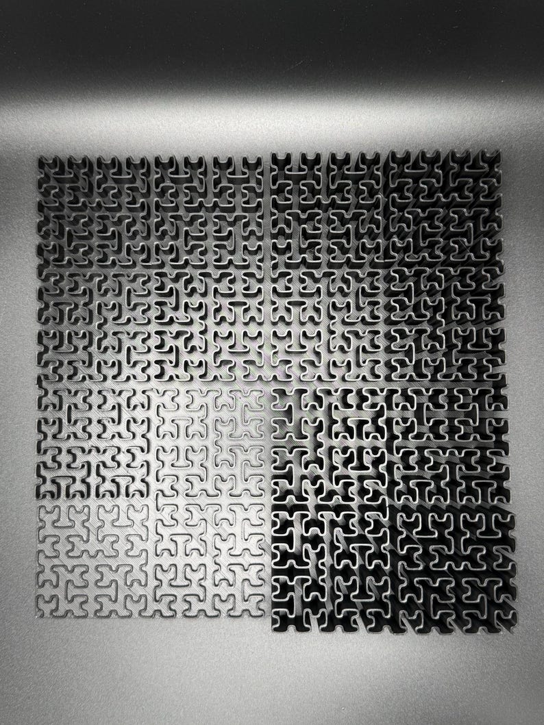 May include: A close-up of a metal surface with a repeating pattern of interlocking puzzle pieces. The surface is divided into four sections, with the top two sections appearing darker than the bottom two sections.