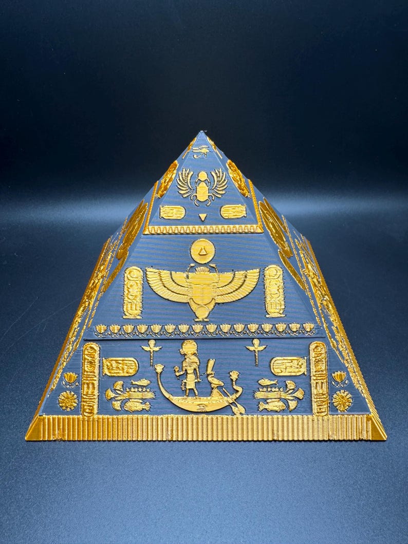 Puede incluir: Una pir&aacute;mide dorada detallada con intrincados jerogl&iacute;ficos y s&iacute;mbolos egipcios sobre una superficie azul oscuro. La pir&aacute;mide presenta un dise&ntilde;o en capas con varias figuras y patrones en relieve, mostrando el arte del antiguo Egipto.