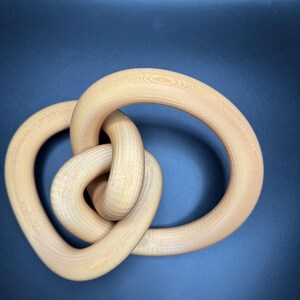 May include: A wooden sculpture in the shape of a knot. The sculpture is made of light brown wood and has a smooth, polished finish.