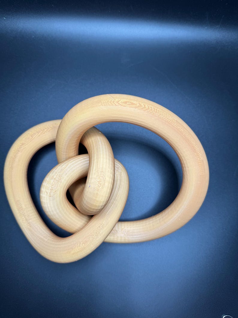 May include: A wooden sculpture in the shape of a knot. The sculpture is made of light brown wood and has a smooth, polished finish.
