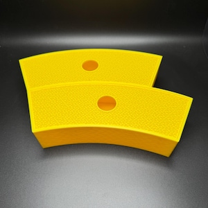 May include: Two bright yellow, curved containers with a textured surface and a circular hole in the center. The containers are stacked on top of each other, with a dark background.