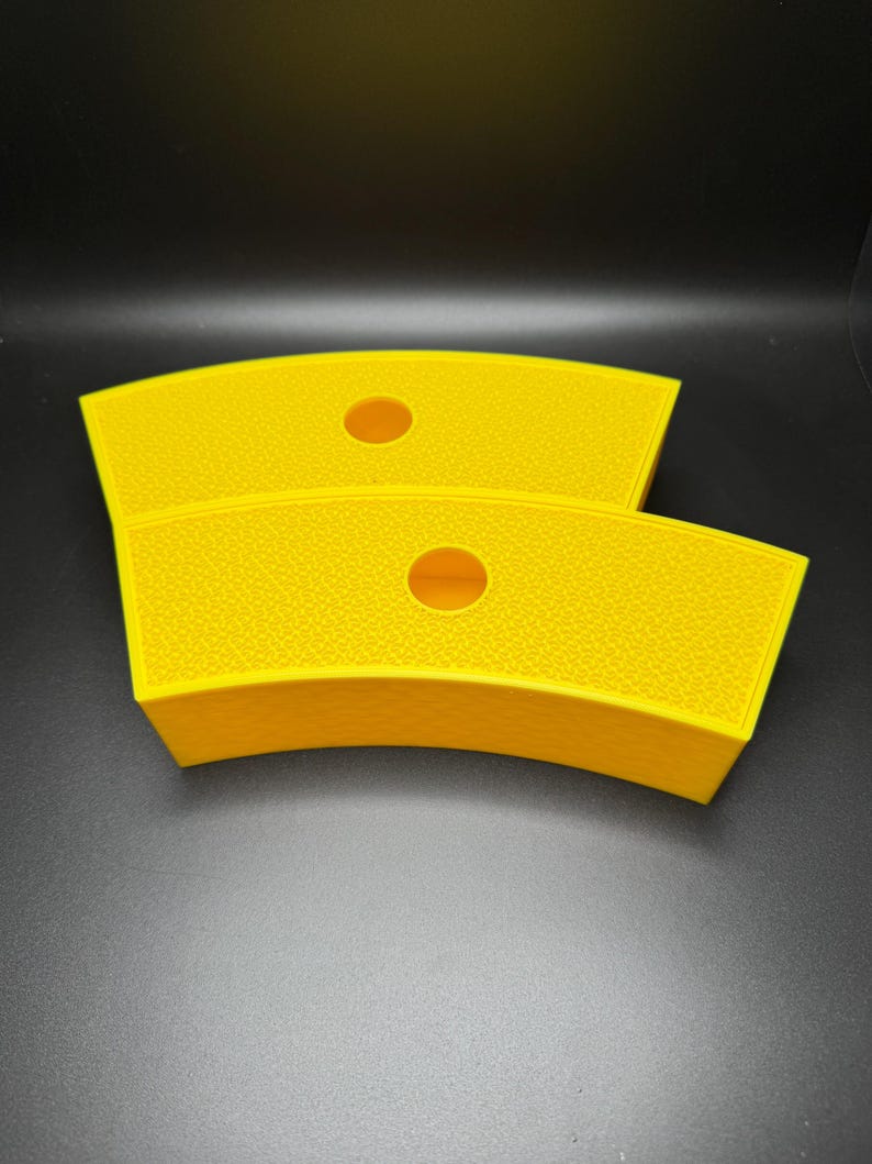 May include: Two bright yellow, curved containers with a textured surface and a circular hole in the center. The containers are stacked on top of each other, with a dark background.