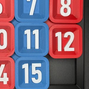 Pu&ograve; includere: Primo piano di un tabellone di gioco blu e rosso con numeri bianchi. I numeri sono 6, 7, 8, 10, 11, 12, 14 e 15.