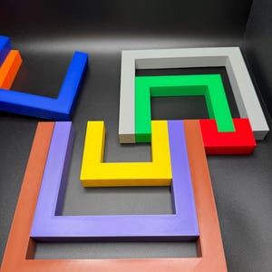 May include: A collection of colorful, geometric puzzle pieces in various shapes and sizes. The pieces are in shades of blue, orange, yellow, green, red, gray, purple, and brown. The puzzle pieces are arranged on a dark surface.