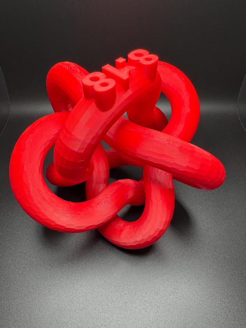 May include: A red 3D printed sculpture of a knot with the number "81.8" printed on it.