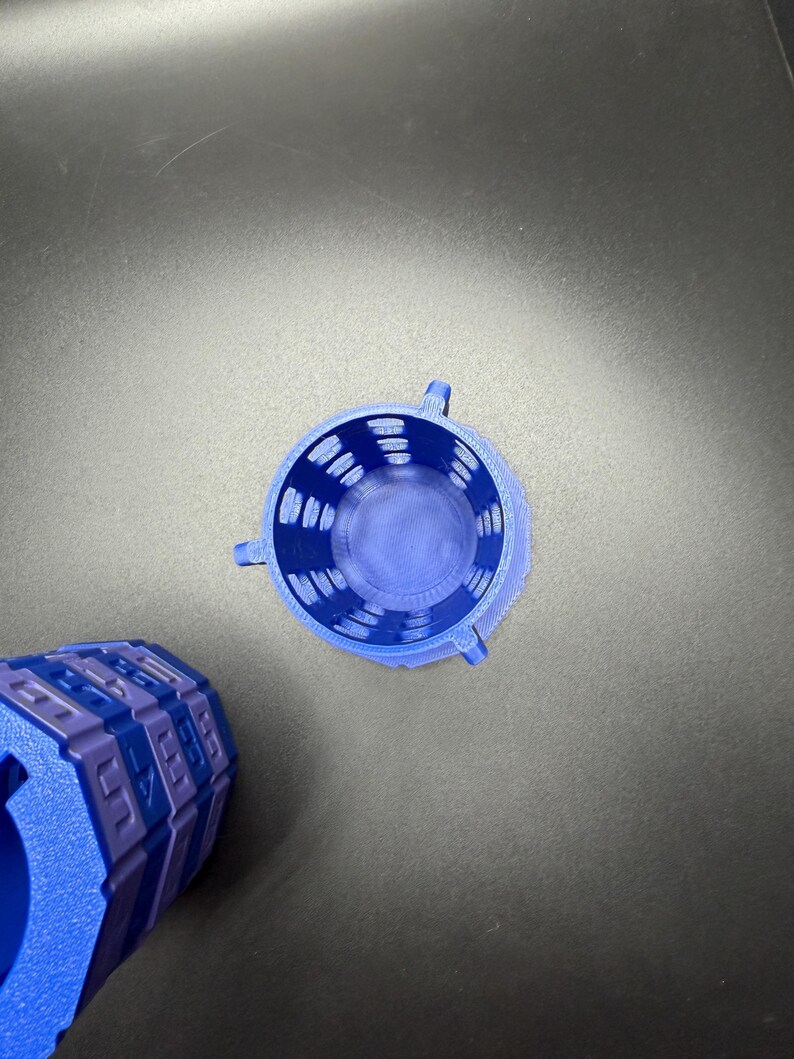 May include: A top-down view of a blue 3D-printed cylindrical container with a textured surface and three small handles. The container is next to a blue and purple geometric object.