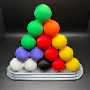 May include: A pyramid-shaped puzzle made of colorful balls. The balls are arranged in a triangular pattern, with the largest ball at the top and the smallest balls at the bottom. The balls are made of a smooth, plastic material and are painted in a variety of colors, including red, green, yellow, orange, purple, white, and black.