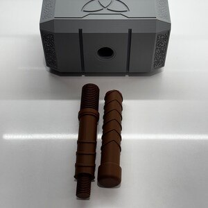 Peut inclure: Un mod&egrave;le en plastique gris du marteau de Thor, Mjolnir, avec un symbole &agrave; trois pointes sur le dessus. Deux pi&egrave;ces en plastique brun sont incluses, l'une avec une extr&eacute;mit&eacute; filet&eacute;e et l'autre avec une extr&eacute;mit&eacute; arrondie.