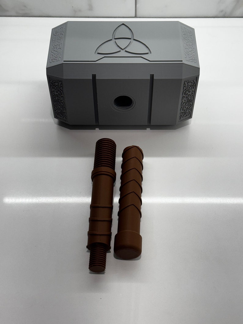 Peut inclure: Un mod&egrave;le en plastique gris du marteau de Thor, Mjolnir, avec un symbole &agrave; trois pointes sur le dessus. Deux pi&egrave;ces en plastique brun sont incluses, l'une avec une extr&eacute;mit&eacute; filet&eacute;e et l'autre avec une extr&eacute;mit&eacute; arrondie.